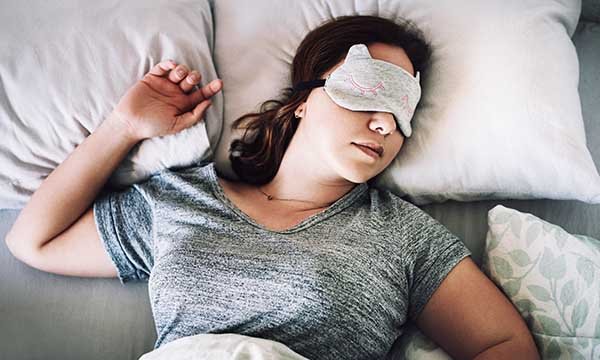 A woman lying in bed asleep, wearing an eye mask to prevent sleep disturbance due to light levels