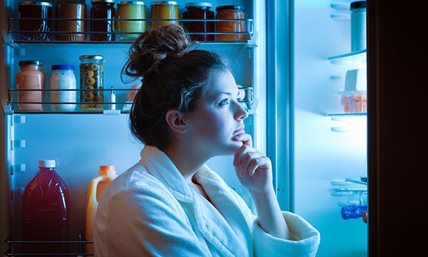 A woman standing looking at the contents of a fridge, choosing what to eat and drink