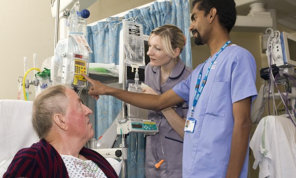 Nursing student delivers bedside care to a man in hospital, under supervision of a registered nurse