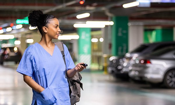 A nurse in uniform in an underground car park, with parked cars around her. Free parking for staff is an initiative some workplaces have implemented to encourage staff to stay