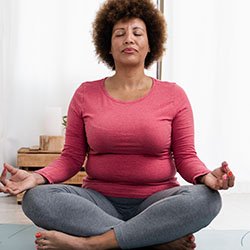 A woman sits crossed-legged with her eyes shut, engaged in meditation, which can help to manage symptoms of perimenopause