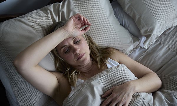 A woman lies in bed with her arm across her forehead, unable to sleep, as is common for women experiencing perimenopause symptoms