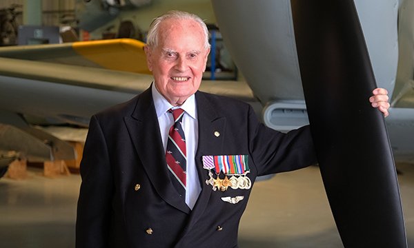 Colin Bell, wearing his war service medals, holding the propeller of a plane