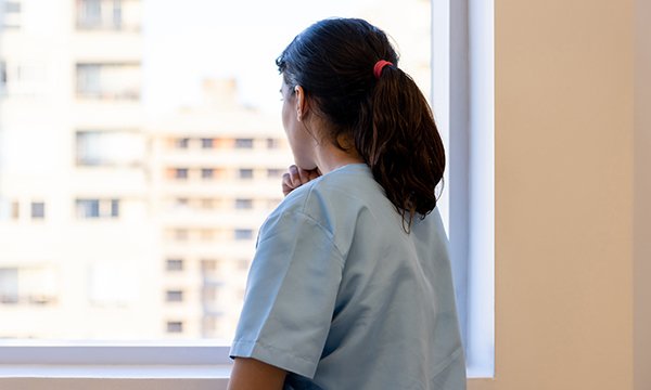 A young female care worker standing at a window and resting her chin on her hand 