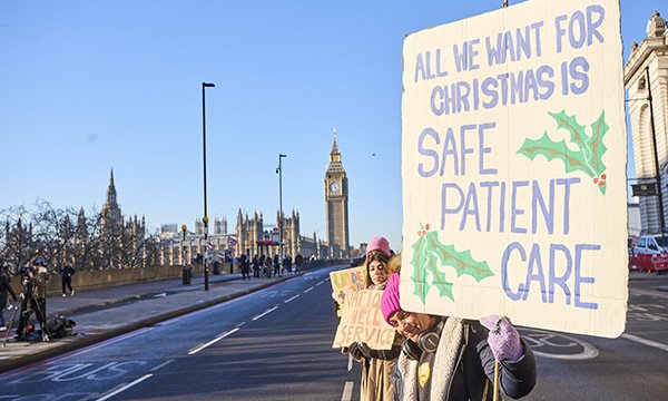 Nurses with homemade strike sign on brown cardboard stand on approach to Westminster Bridge with Houses of Parliament and Big Ben in the background