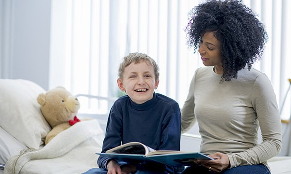 Picture shows a woman and a boy sitting on a hospital bed, reading a book together. Nurses interviewed about caring for children with learning disabilities in acute settings stressed the need to be adaptable and flexible