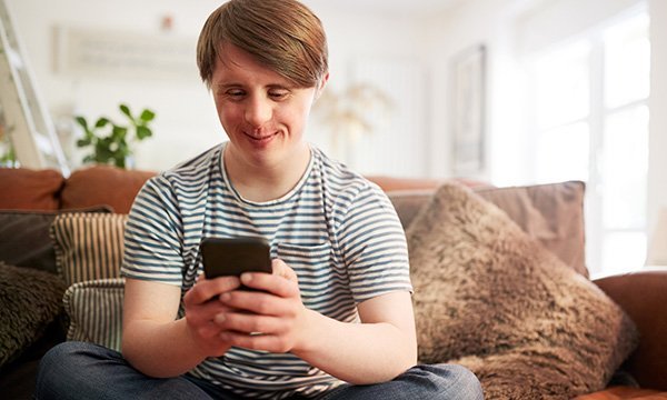 Picture shows a young male holding a smartphone. This article reports on a study showing social media presents opportunities for people with learning disabilities, but those supporting them must be alert to risks including cyberbullying and exploitation.