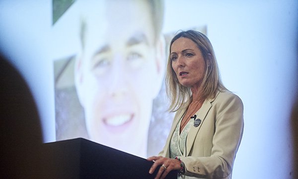 Image show campaigner Paula McGowan speaking at a conference with an image of her son Oliver behind her