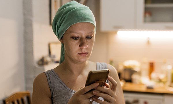 Picture shows a young woman wearing a headscarf after radiation therapy looking pensive as she uses her phone. A self-help app called Untire can help cancer patients and survivors regain their energy.