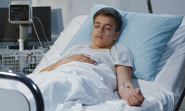 Picture shows a teenage boy lying in a hospital bed with his eyes closed.