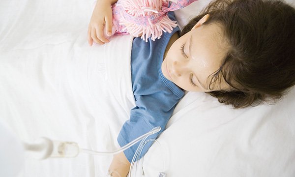 Picture shows a child lying in a hospital bed with an IV line attached to her arm