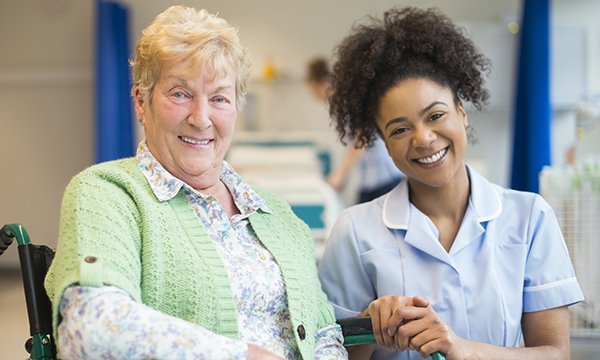 Nurse crouches down to be at same level as woman seated in a wheelchair