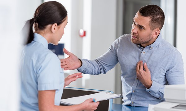 Man adopts aggressive stance and gesticulates angrily as he talks angrily to female nurse 