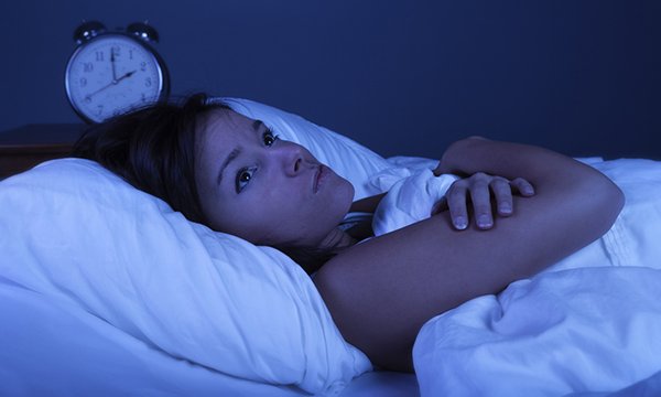 Picture shows a young woman suffering from insomnia with blue nighttime effect. This research digest looks at three studies relating to sleep health, insomnia and cognitive behavioural therapy as a primary care intervention.