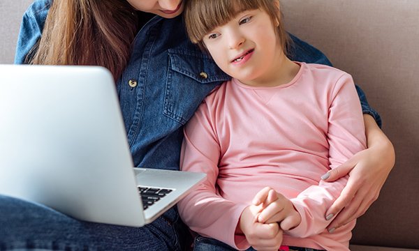 Young child with learning disabilities being guided by her parent to use virtual technology