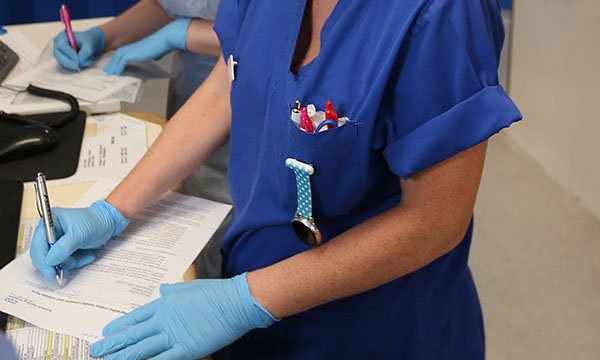 Picture of inappropriate glove use - a nurse wearing gloves fills in a form