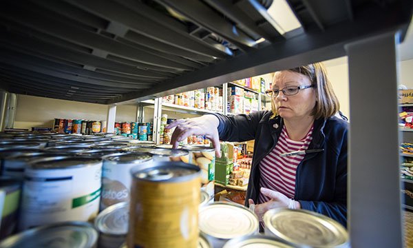 Picture of a volunteer in a food bank taking canned food off a shelf